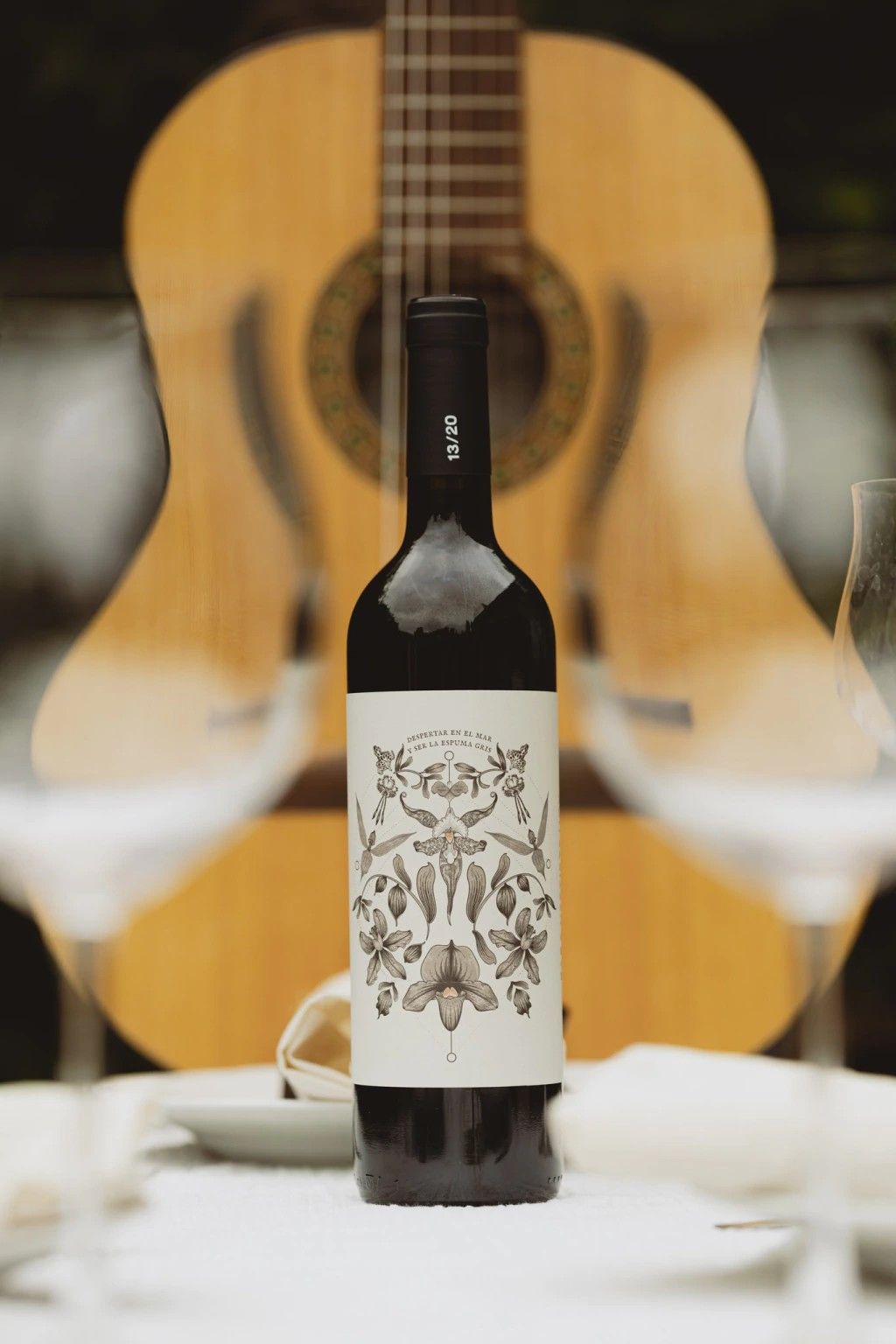 Botella de Para Vestirte Hoy sobre una mesa, delante de una guitarra